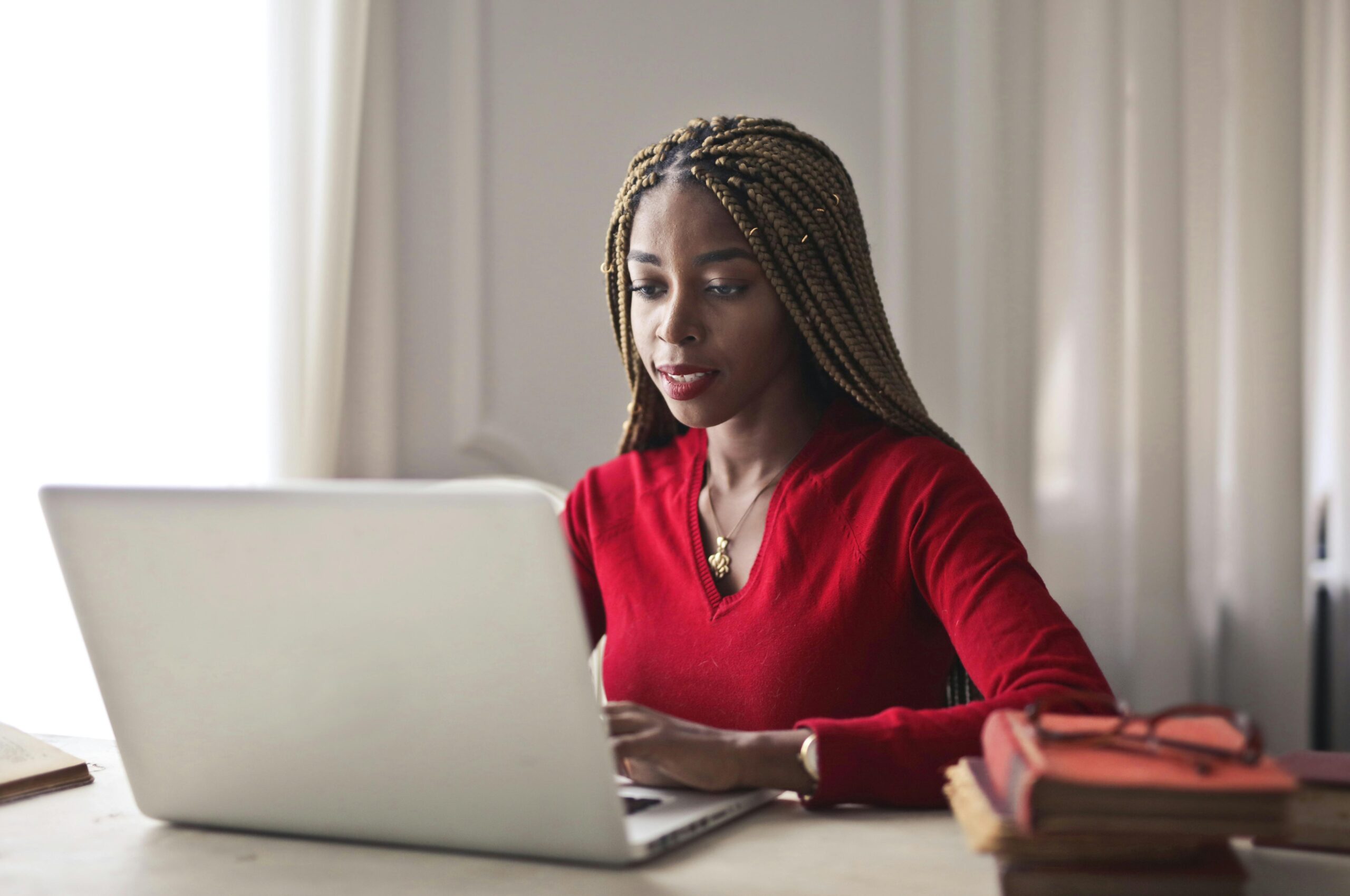 Confident woman in a red sweater working on a laptop in a bright, organized workspace.
